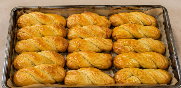 Twisted braided bread rolls with a glossy golden-brown glaze, arranged in rows on a parchment-lined metal baking tray.