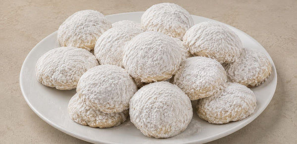 A white ceramic plate piled with powdered sugar-coated cookies on a light beige textured surface.
