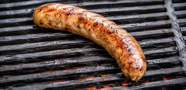 A grilled sausage or brisket resting on black grill grates with visible orange embers underneath.